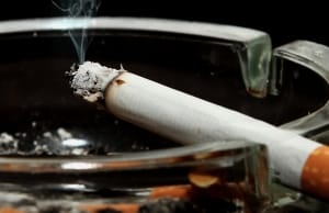 Burning in Ashtray – M Tobacco Verdict - Ferraro Law Firm Lit cigarette resting on the edge of a glass ashtray with smoke rising, symbolizing tobacco-related lawsuits like R.J. Reynolds v. Clay.