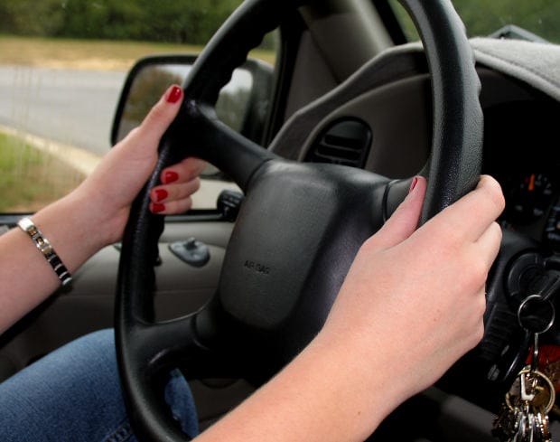 Close-up of a person’s hands gripping a black car steering wheel with a key in the ignition.