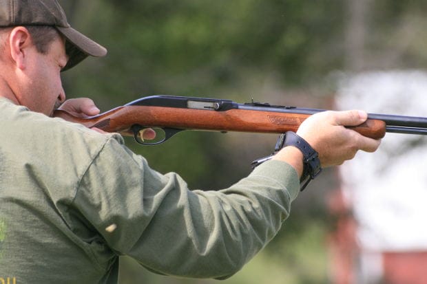 Hunter Aiming Rifle - Ferraro Law Firm A hunter in a green shirt aiming a rifle outdoors, representing treestand hunting accident litigation in Bradley v. Ameristep, Inc.
