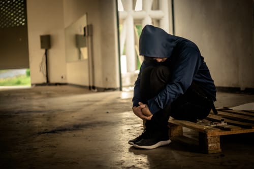 Person in a hoodie sitting alone in a dark, empty space, symbolizing the physical and emotional toll of opioid addiction.