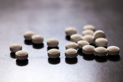 Prescription Opioid Pills on Table - Ferraro Law Firm Close-up of several small, round white prescription opioid pills scattered on a dark surface.