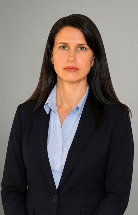 Professional woman in a navy blazer and light blue shirt posing against a gray backdrop.