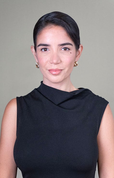 Professional portrait of a woman with dark hair, wearing a black sleeveless top and gold earrings, looking at the camera.