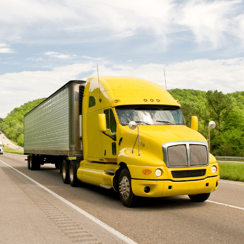 Bright yellow semi-truck driving on a highway surrounded by green hills and blue sky, representing commercial trucking liability questions.