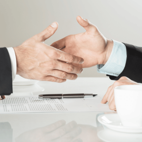Two business professionals shaking hands over a signed contract, symbolizing agreement, trust, and commitment in a business deal.
