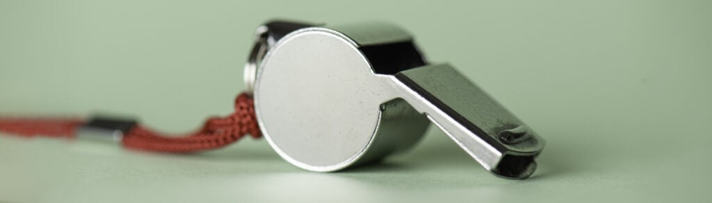 Close-up of a silver whistle with a red cord on a pale green surface.