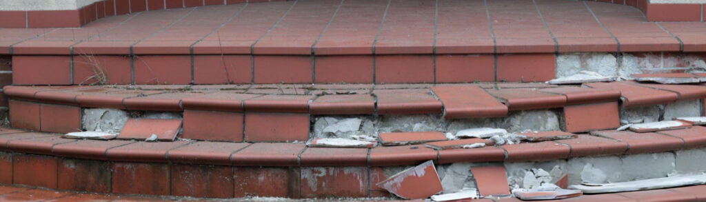 Red tiled stairs in disrepair with missing and broken tiles and rubble on the steps