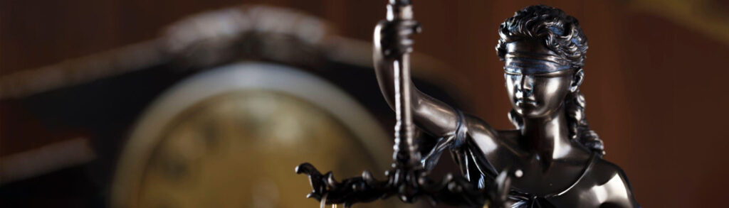 Blindfolded Lady Justice statue holding scales, with a blurred clock in the background, symbolizing law and time