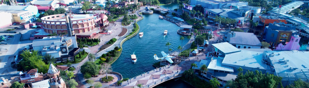 Aerial view of a colorful waterfront amusement park with a central canal, boats, and pedestrian promenades.