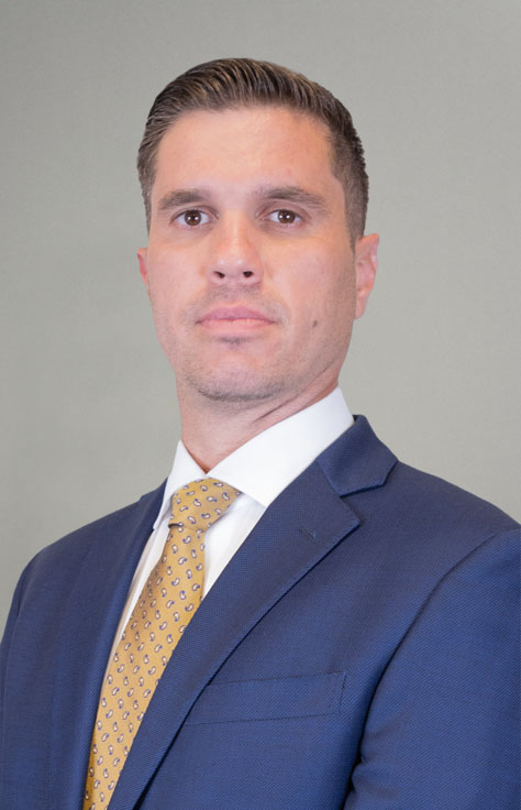 Head-and-shoulders portrait of a man in a navy suit and yellow patterned tie, looking at the camera.