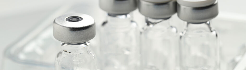 Row of small glass vials with gray metal caps in a laboratory setting.